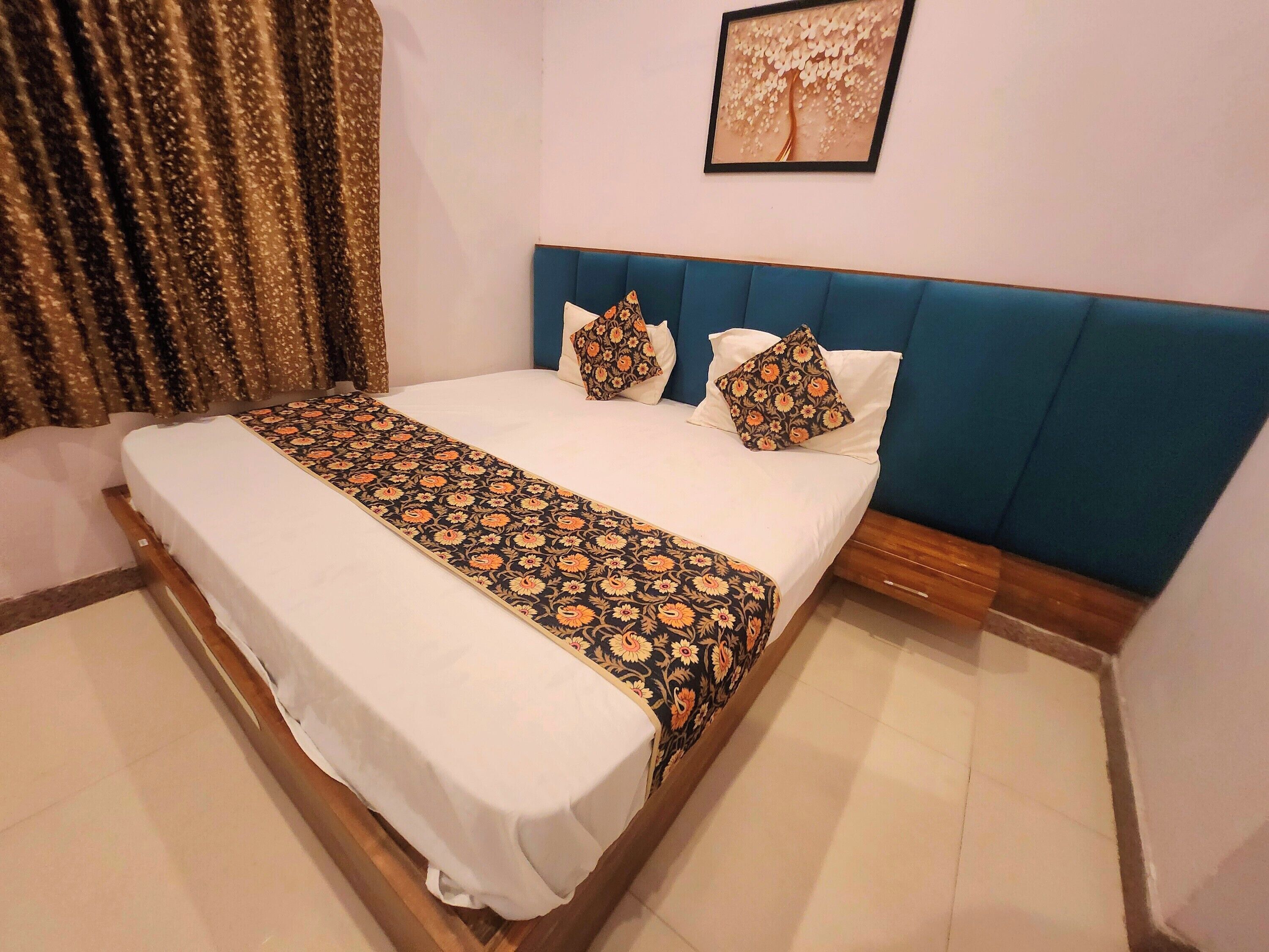 A neatly made bed with a patterned bedspread, a blue upholstered headboard, and a framed picture on the wall.