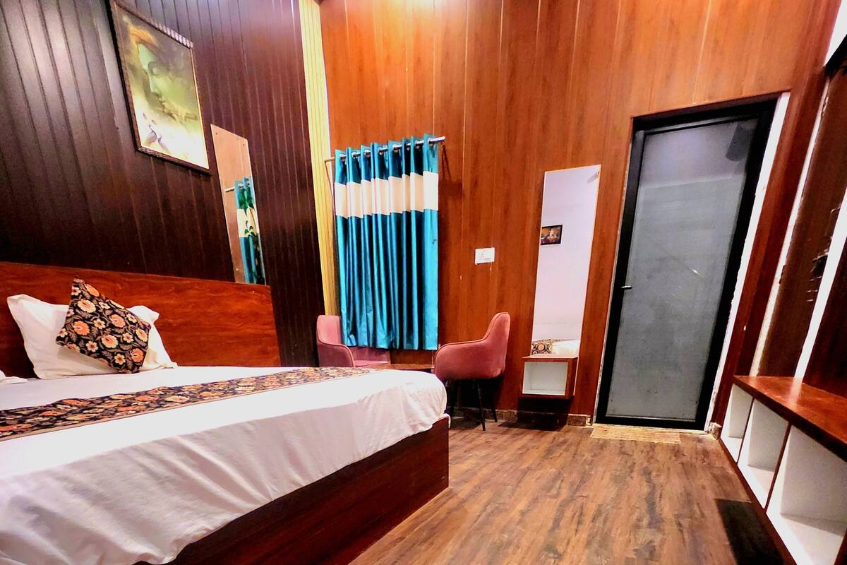 Habitación de hotel con piso de madera, cama con almohada estampada, escritorio con silla y una puerta.