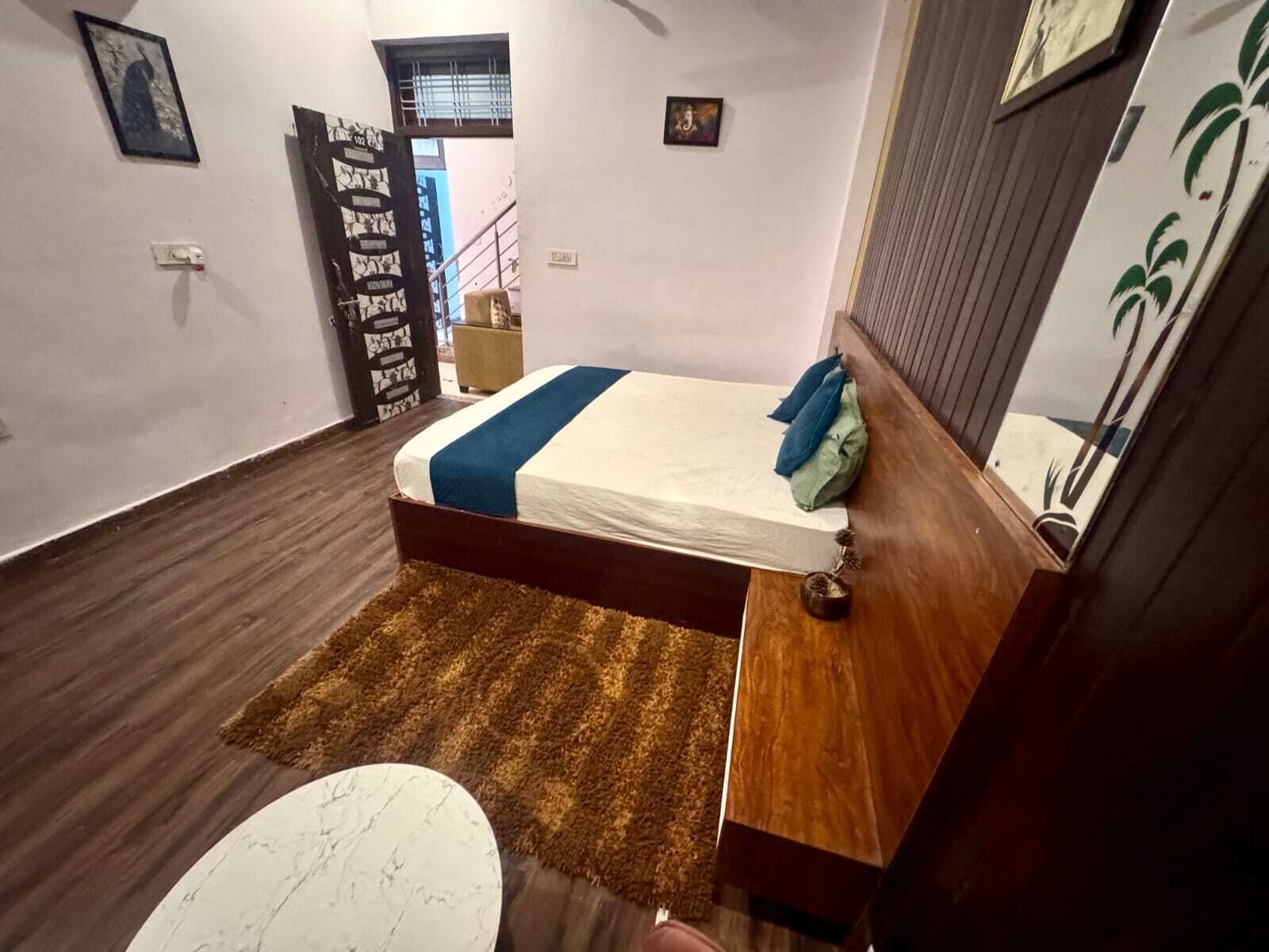 Een slaapkamer met een bed, een houten hoofdbord, een bruin vloerkleed, een marmeren tafeltje en een deur met decoratief patroon.