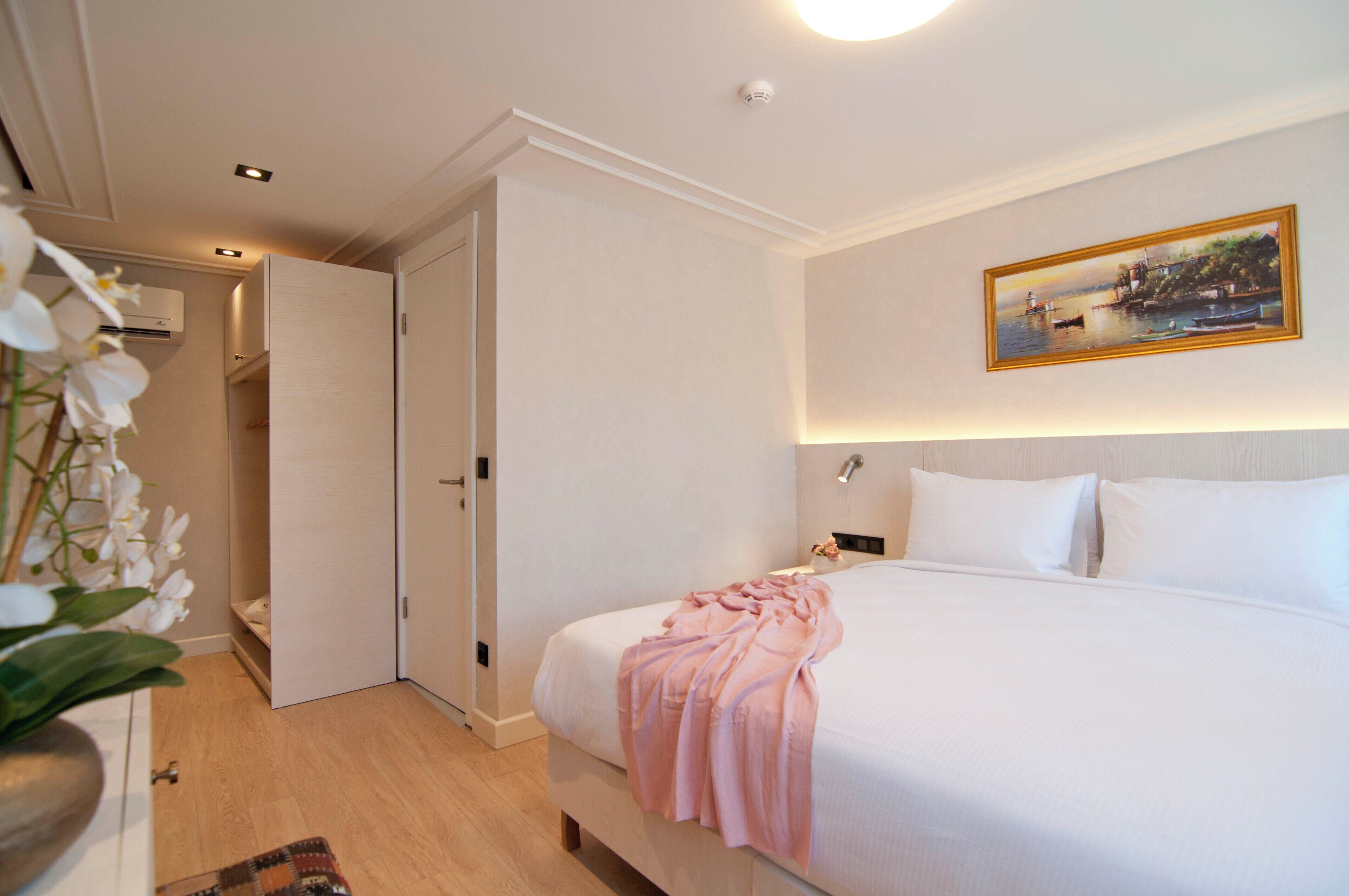 A hotel room with a bed, a painting on the wall, and a door leading to another room.