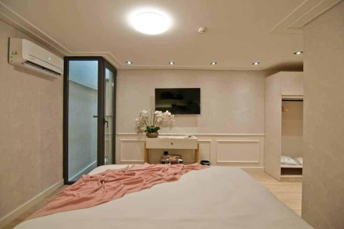 A bedroom with a bed, a bedside table, a mirror, and a wall-mounted TV.