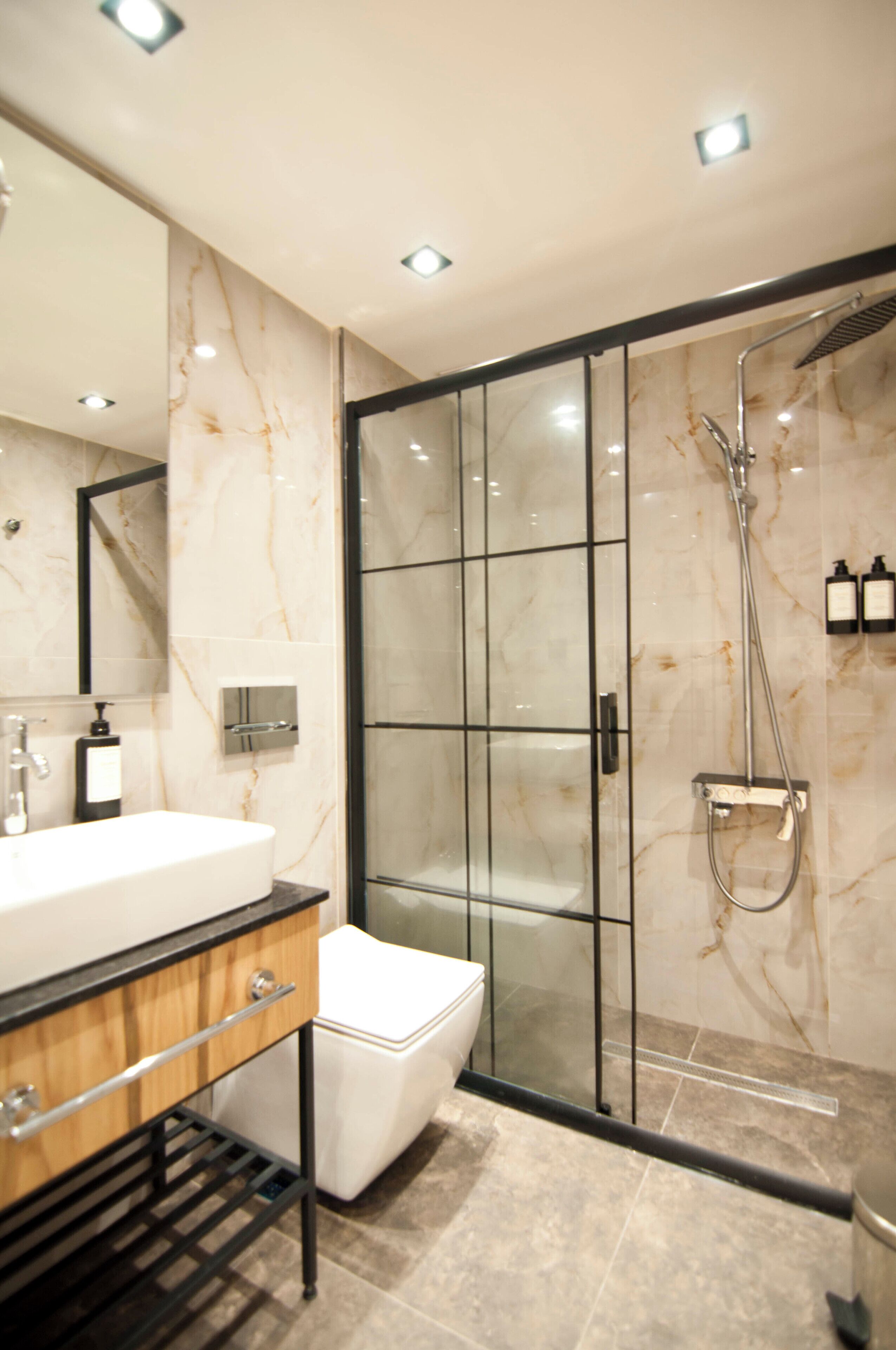 Une salle de bain moderne avec une douche à parois de verre, un lavabo blanc et un mur recouvert de carreaux de marbre.