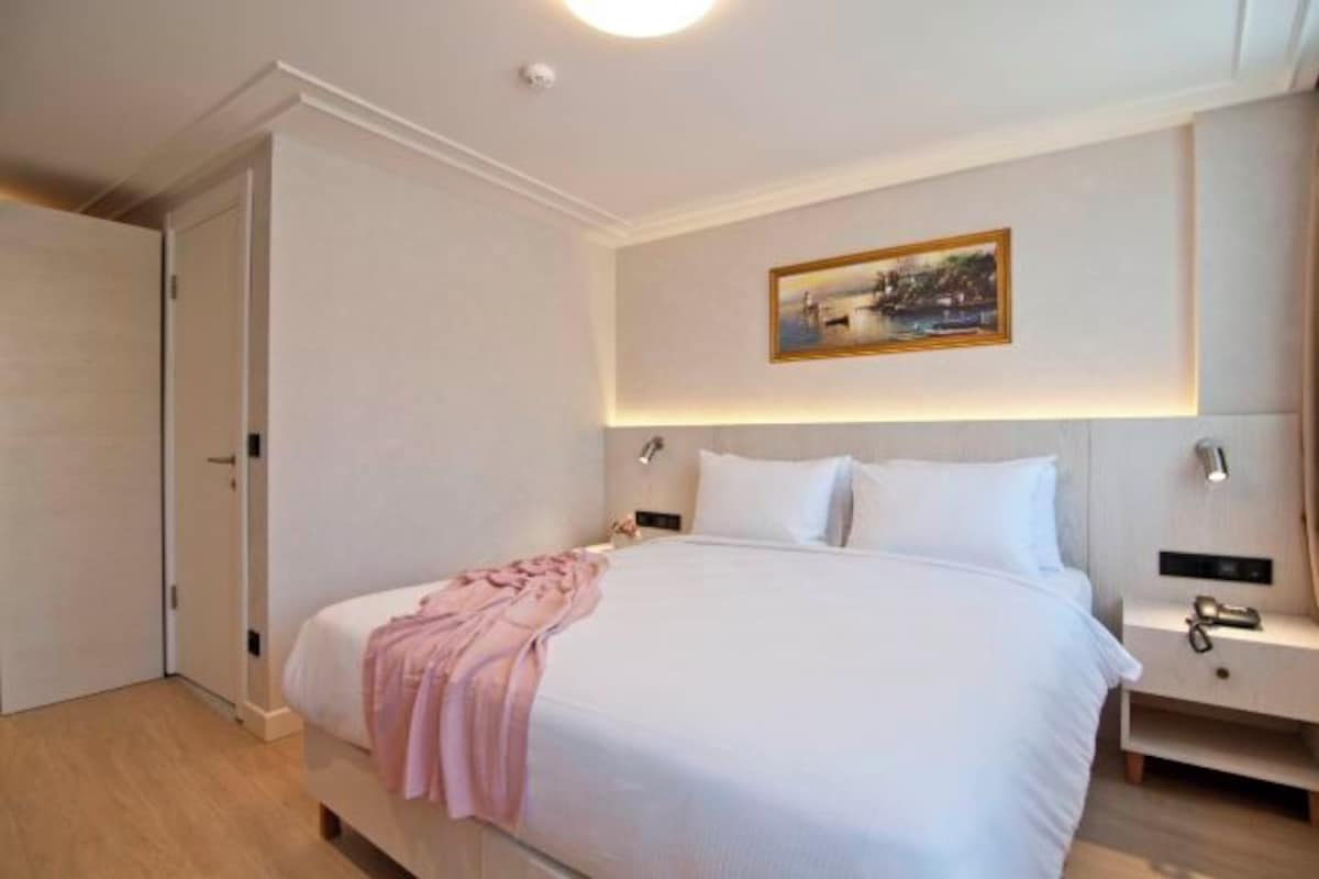 A hotel room with a large bed, bedside tables, a painting on the wall, and a door.