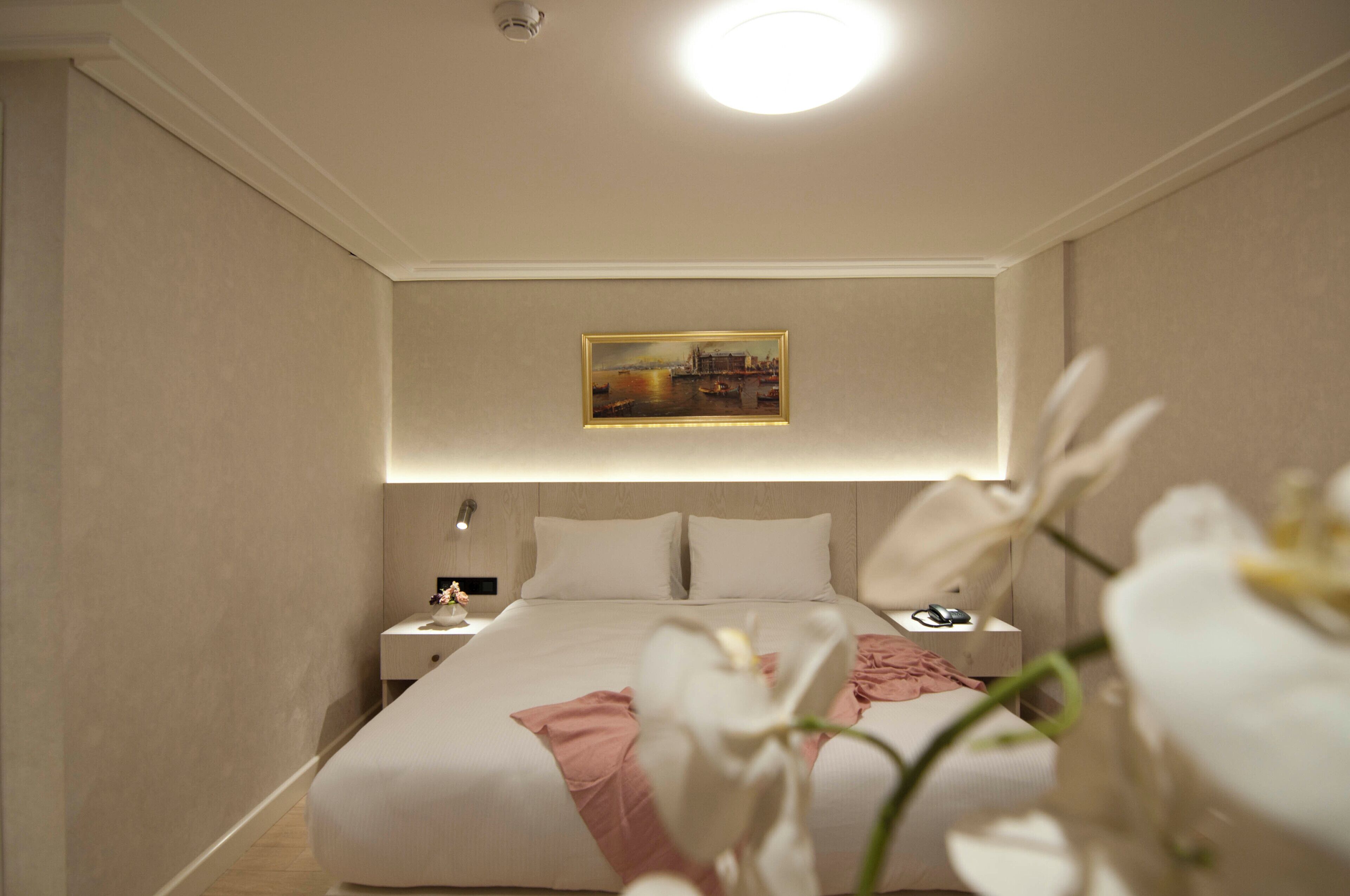 Una habitación de hotel con una cama bien hecha, una mesita de noche con una lámpara y un cuadro en la pared.