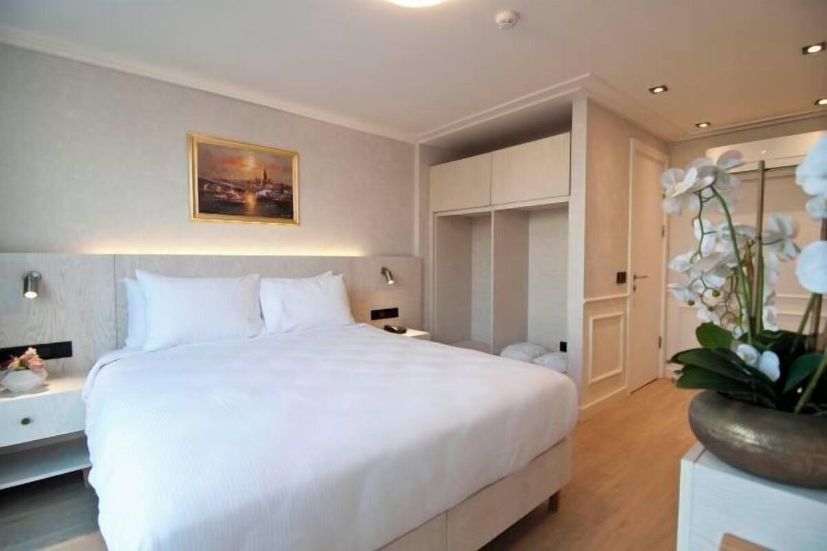 A hotel room with a large bed, bedside tables, a wardrobe, and a painting on the wall.
