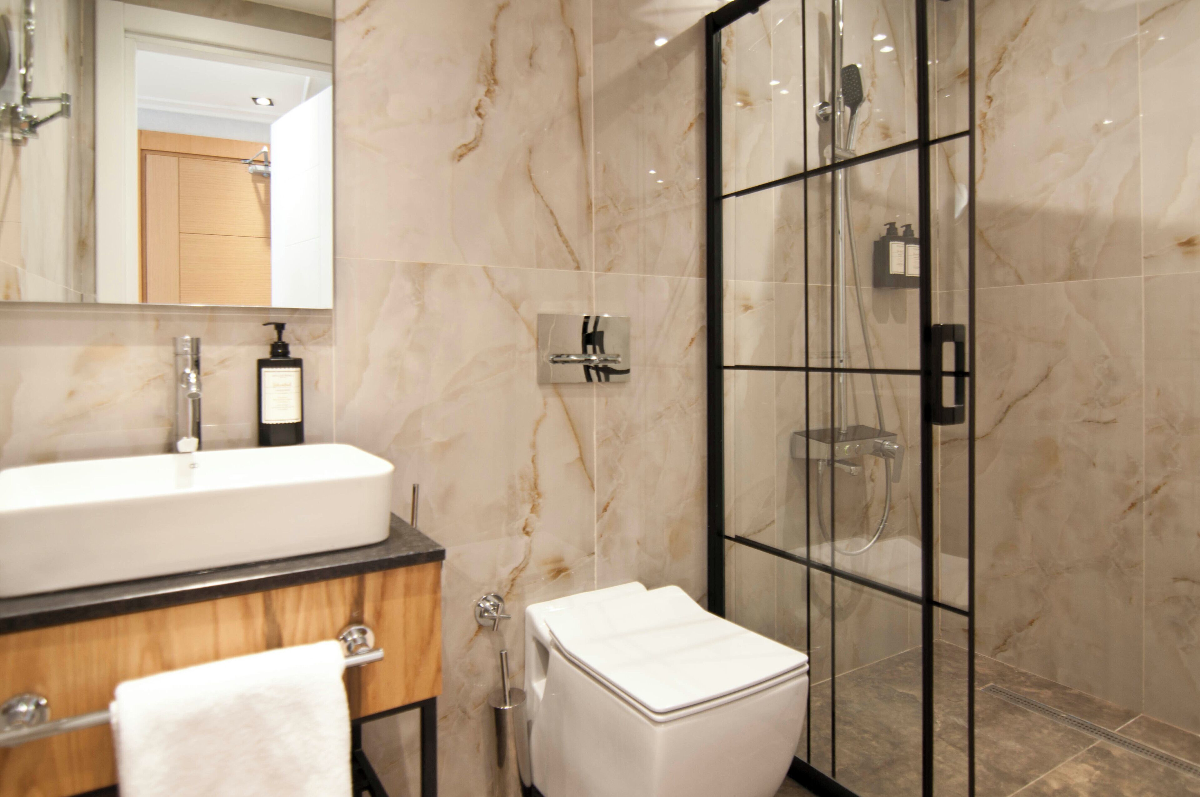 A modern bathroom with a marble vanity, a glass shower enclosure, and a toilet.