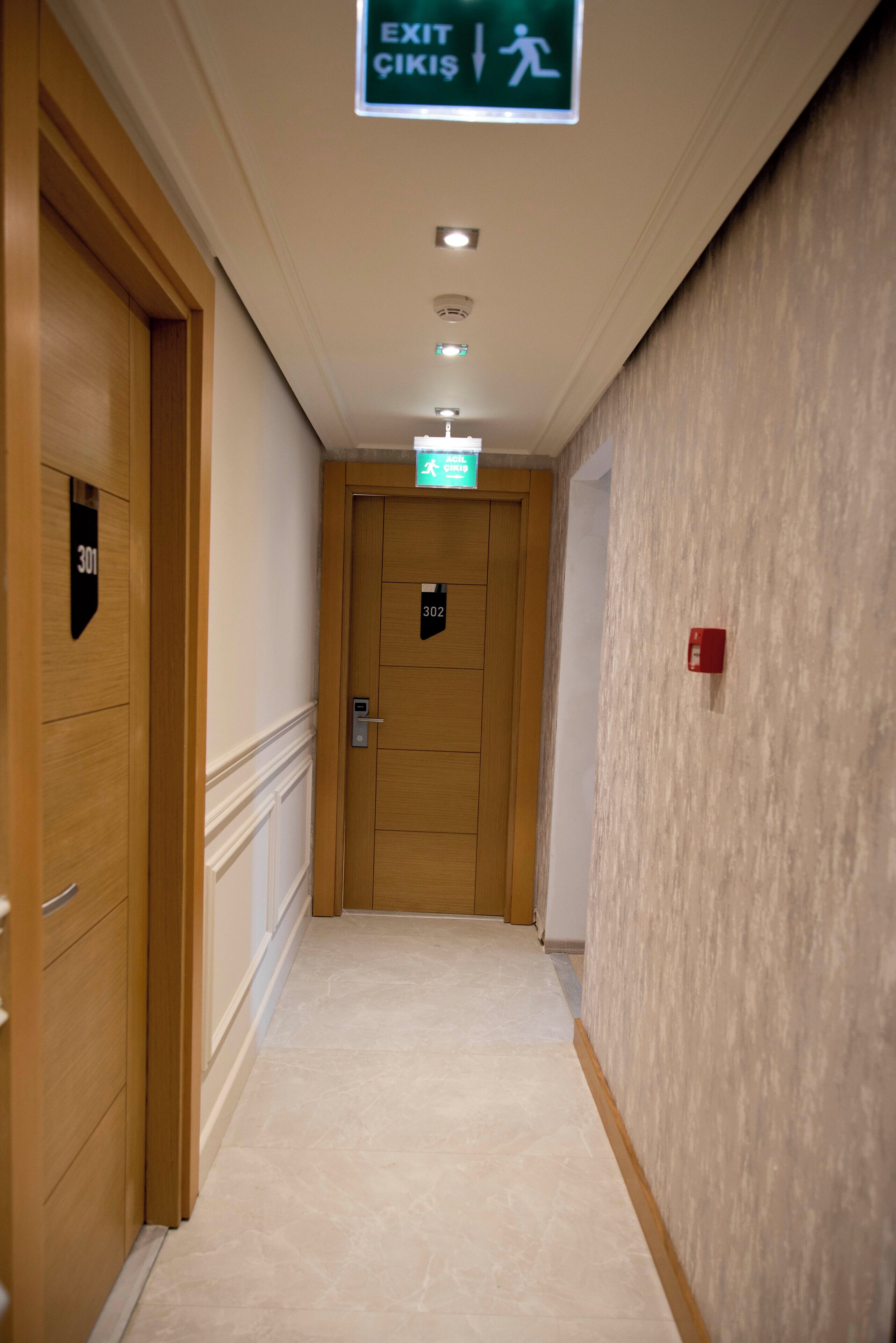 Ein Hotelkorridor mit Holztüren, mit den Nummern 301 und 302, und einem Hinweisschild für den Notausgang.
