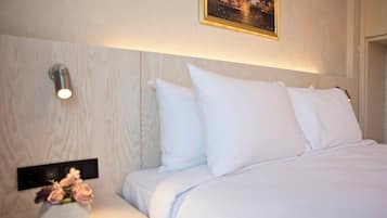 A hotel room with a wooden headboard, white bedding, a bedside table with a vase of flowers, and a wall-mounted light fixture.