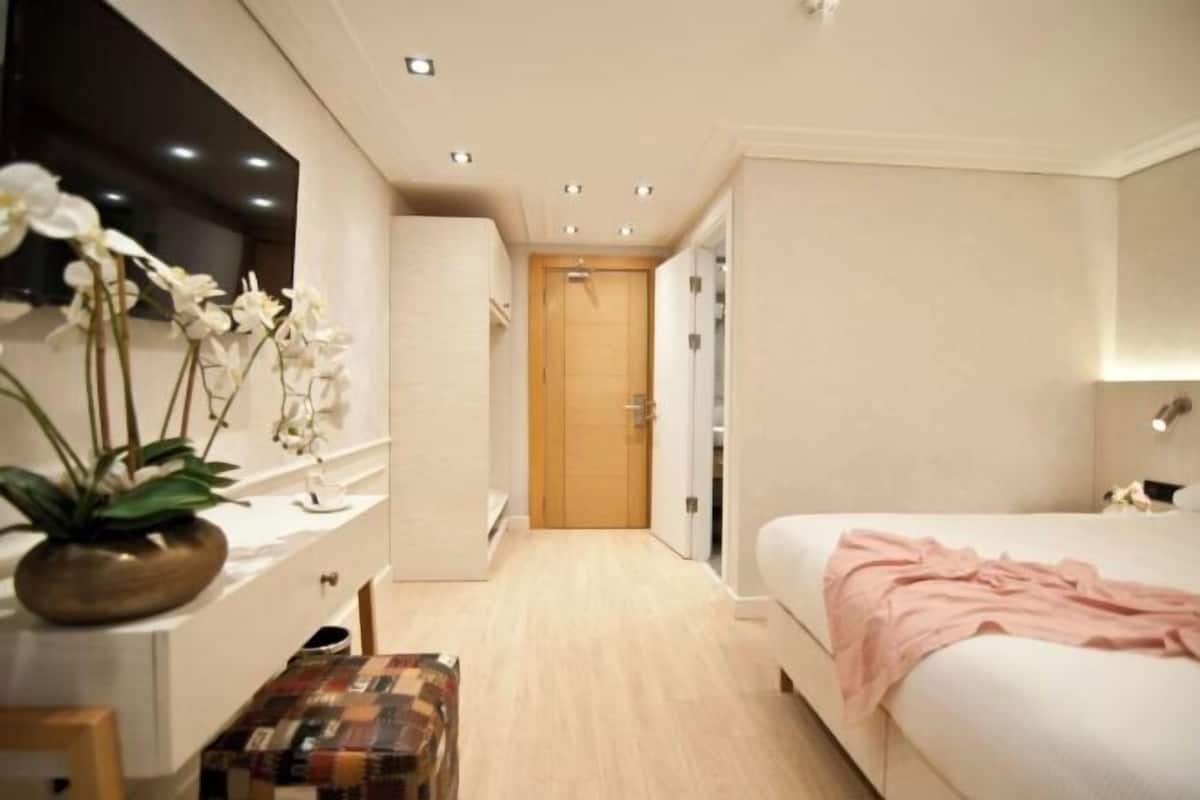 A bedroom with a bed, a bedside table, a mirror, a wardrobe, and a door leading to another room.