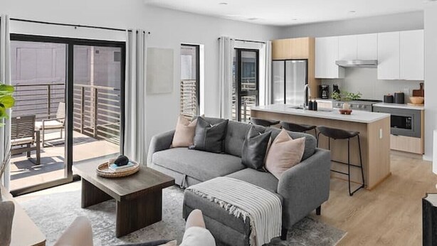A modern living room with a grey sofa, a coffee table, and a dining area with a kitchen in the background. - Luxury Penthouse w/ 2 Floors - Pool, Patio, Gym, Walk to Broadway (Nashville)