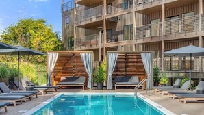 A modern building with a pool area, including lounge chairs and umbrellas. - Luxury Penthouse w/ 2 Floors - Pool, Patio, Gym, Walk to Broadway (Nashville)
