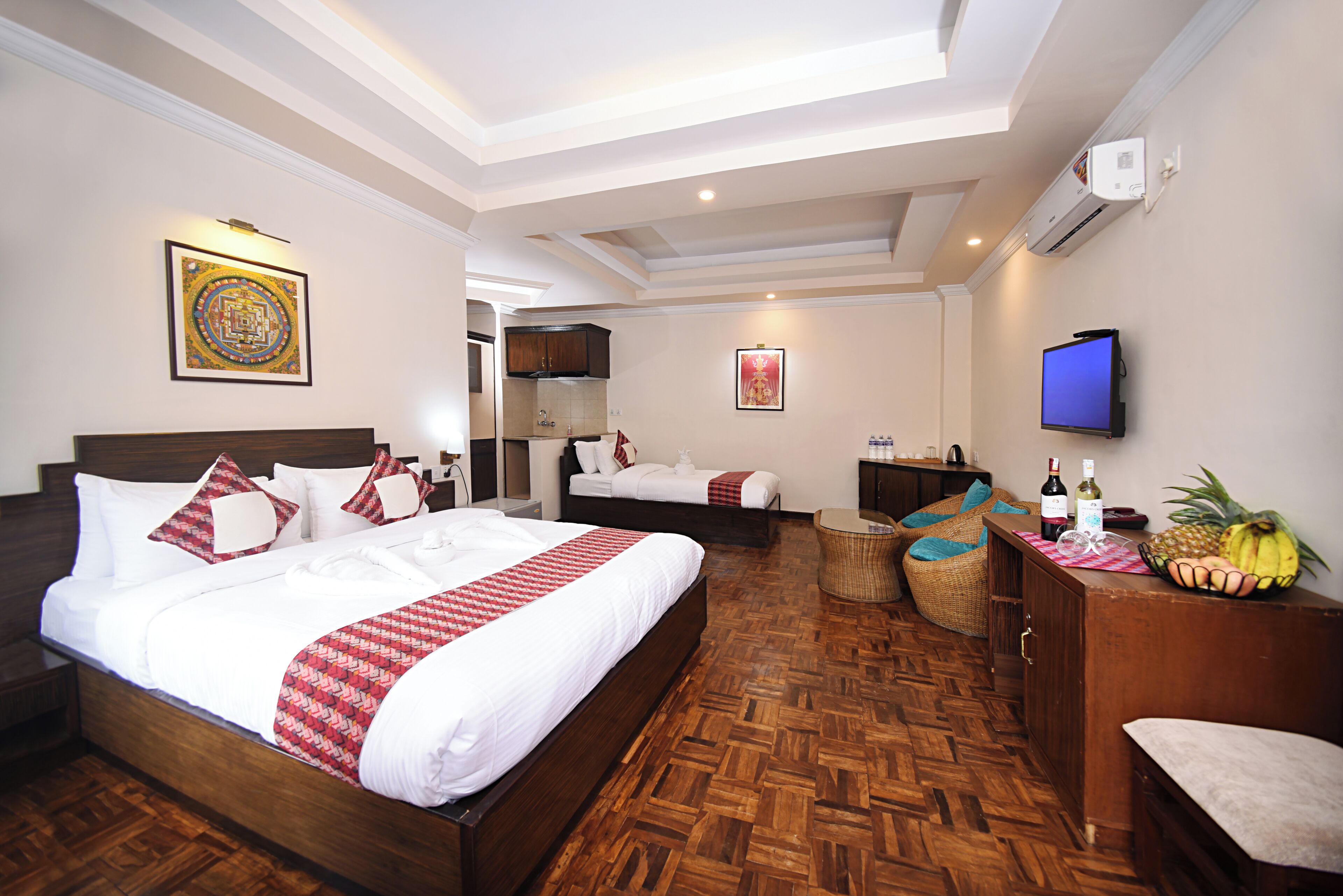 A hotel room with a large bed, a television, a small dining area, and a wall-mounted air conditioner.