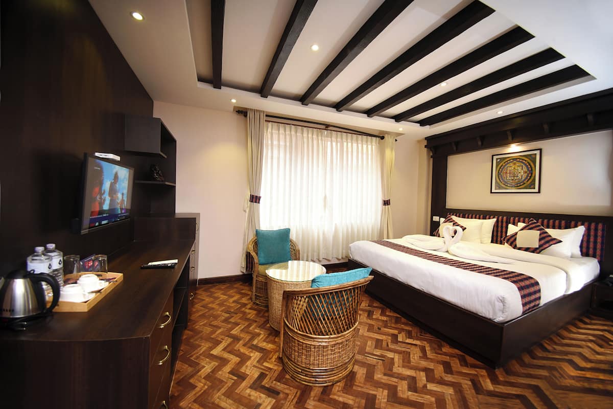 Una habitación de hotel con una cama grande, televisión, escritorio con hervidor y una silla de mimbre.