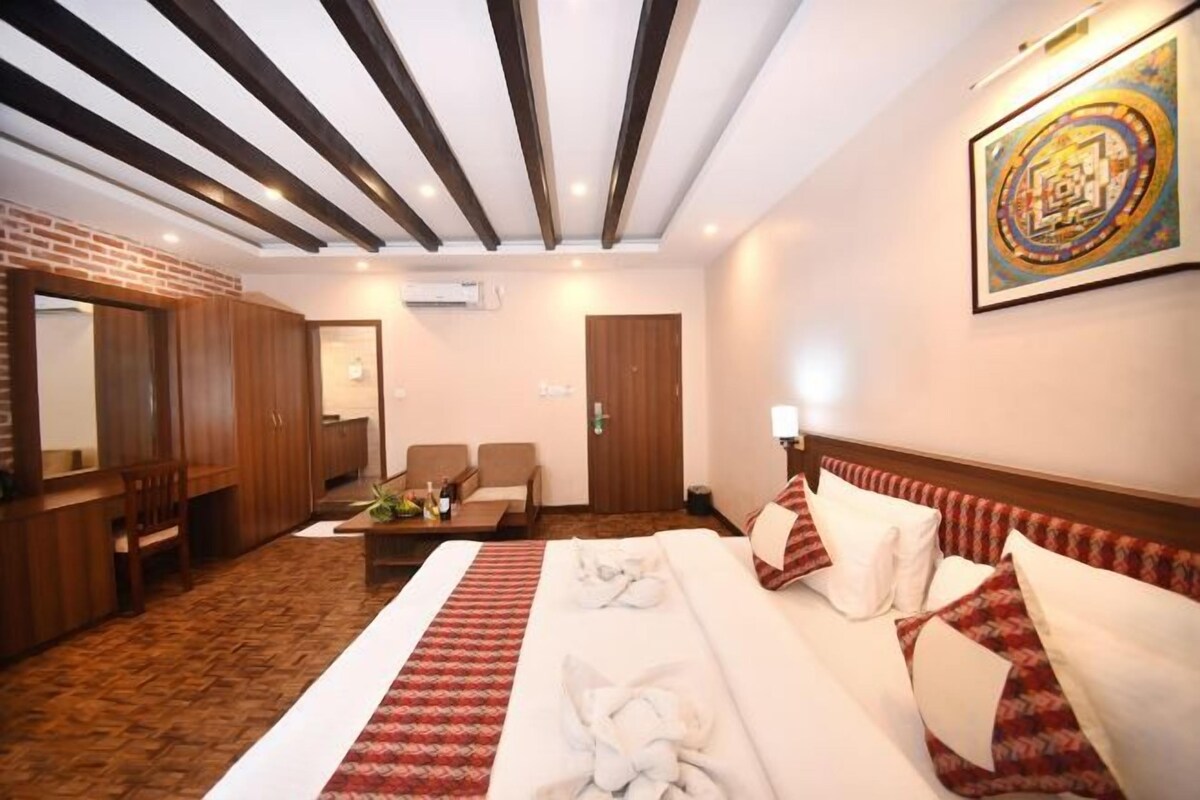 Quarto de hotel com uma cama grande, área de estar com sofá e poltronas, armário de madeira e um quadro na parede.