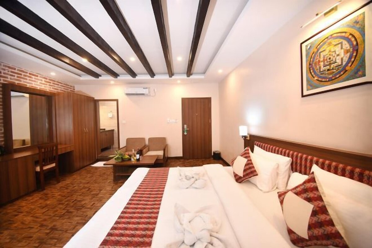 A hotel room with a large bed, a sitting area with a table, a mirror, and a wall-mounted artwork.