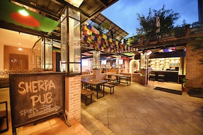 An outdoor seating area of a pub with brick walls and wooden tables. - Skye Inn Kathmandu (Kathmandu)