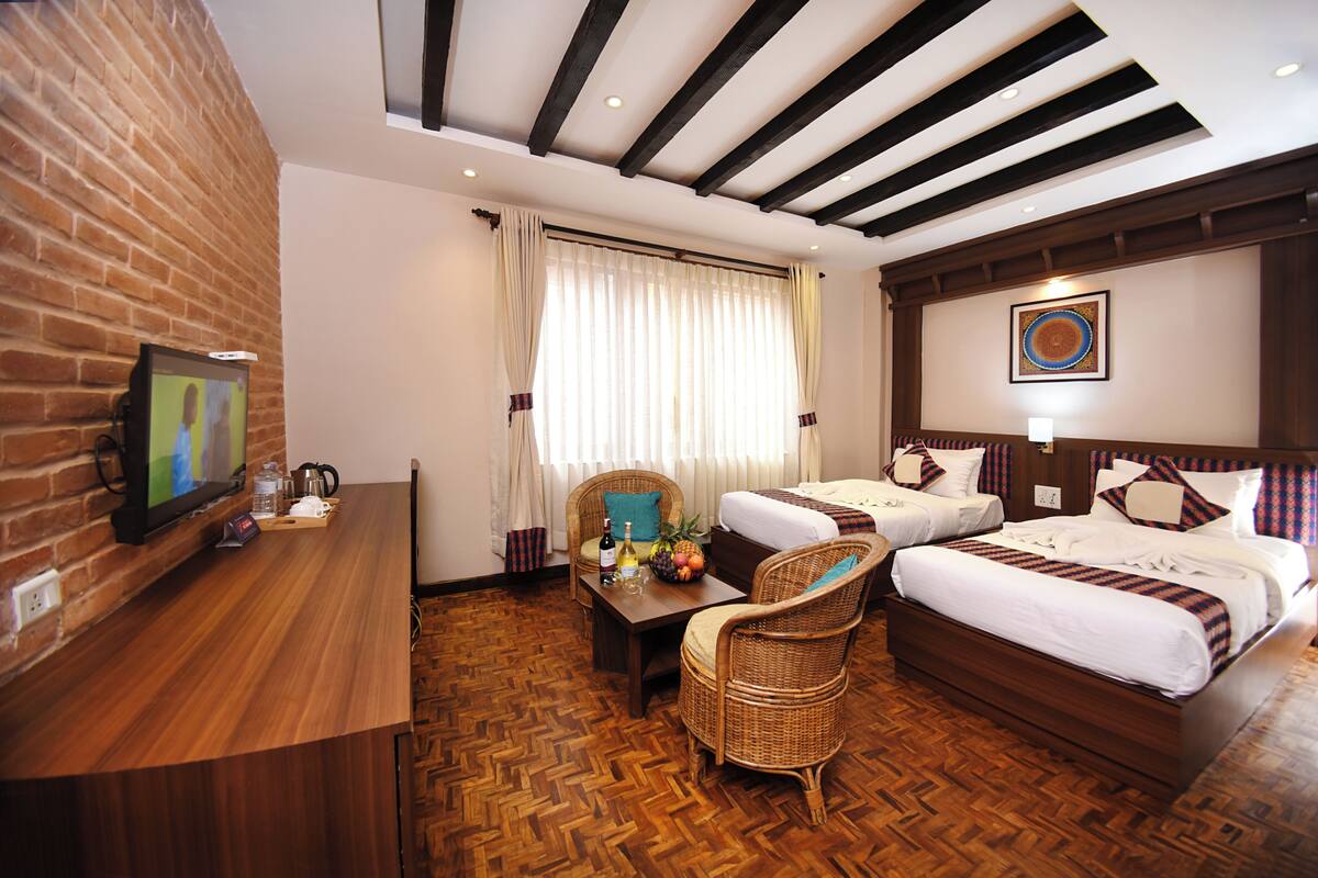 Una habitación de hotel con piso de madera, dos camas individuales, un sofá, un televisor y una cafetera.