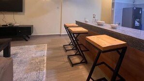 A modern kitchen with a bar area, wooden stools, and pendant lighting. - Lux Suites Kipande Family Apartments (Nairobi)