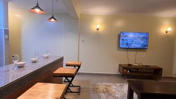A modern living room with a bar area, wooden tables, a leather sofa, a flat-screen TV, and a patterned rug.