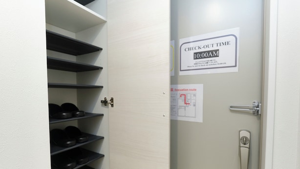 Egy ajtó, amelyen egy tábla jelzi a kijelentkezési időpontot (10:00), egy fém kilincs és egy kis méretű evakuációs útvonal-vázlat található rajta.