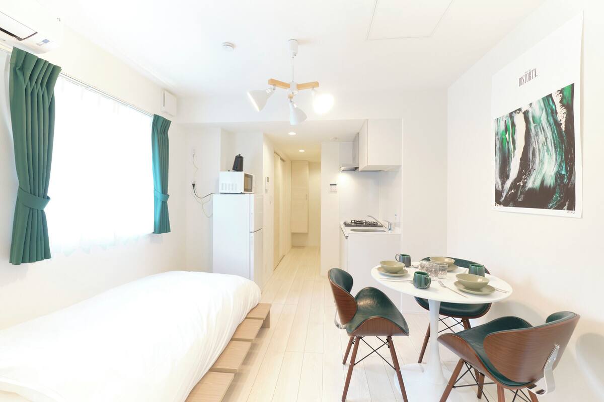 A modern room with a bed, a dining table with chairs, a kitchen area, and a ceiling fan.