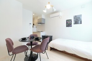 A modern room with a bed, a dining table with chairs, a kitchen area, and wall-mounted air conditioning. - Sugamo Green Heights by Tranova (Tokyo)
