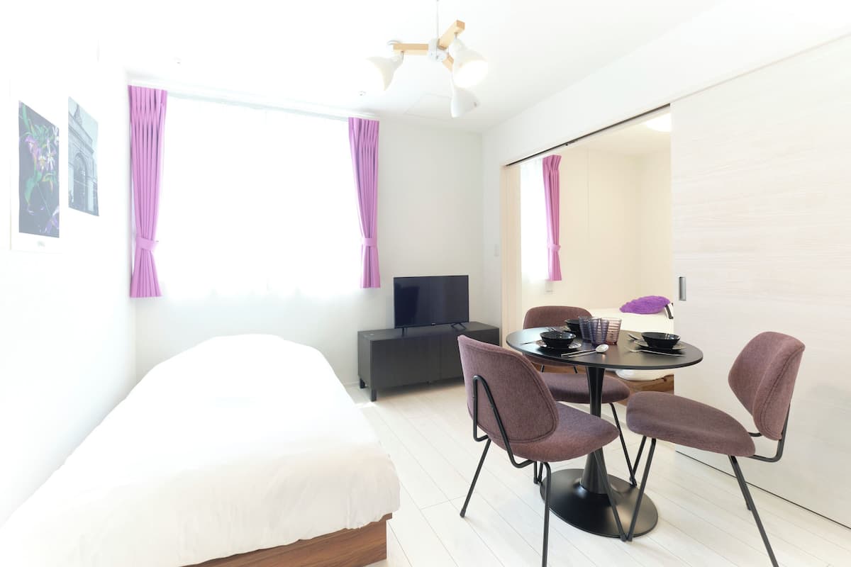 A modern hotel room with a bed, a TV, a dining table with chairs, and a large mirror.