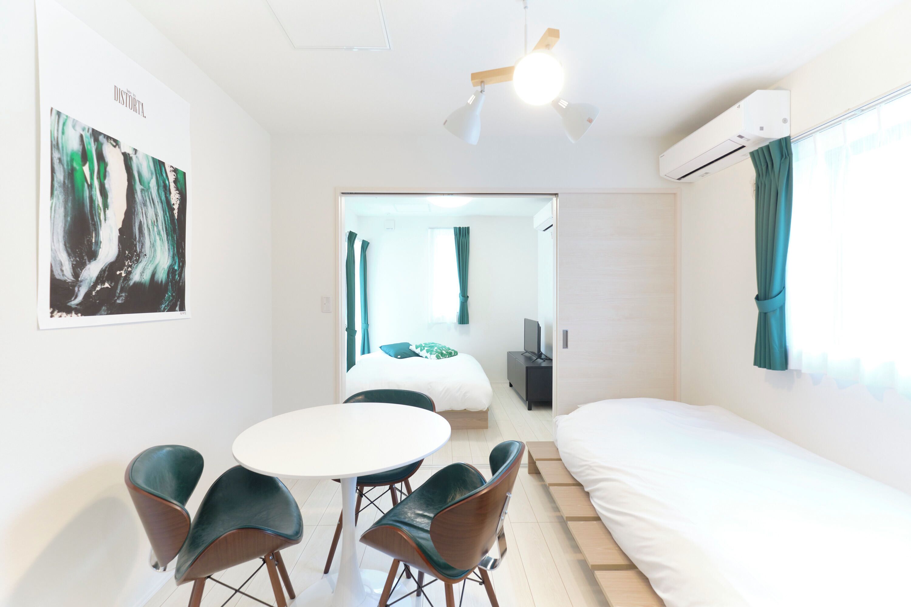 Une chambre d’hôtel moderne, équipée d’un lit, d’une table à manger avec des chaises, d’un ventilateur de plafond et d’un tableau au mur.