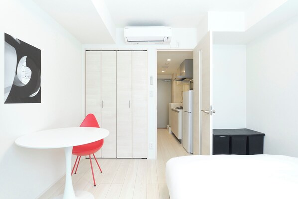 Ett modernt hotellrum med en säng, ett litet bord med en röd stol, en garderob och ett litet kök.