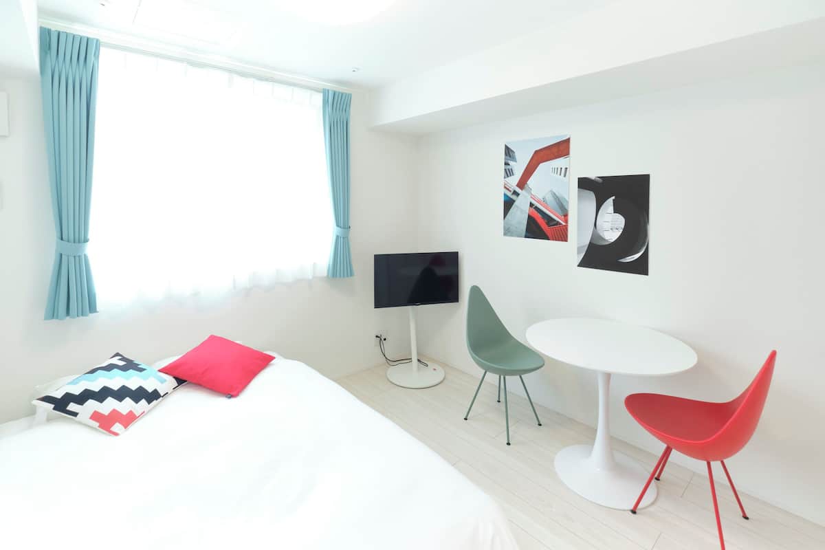 A modern hotel room with a bed, a TV, a small table, two chairs, and artwork on the wall.