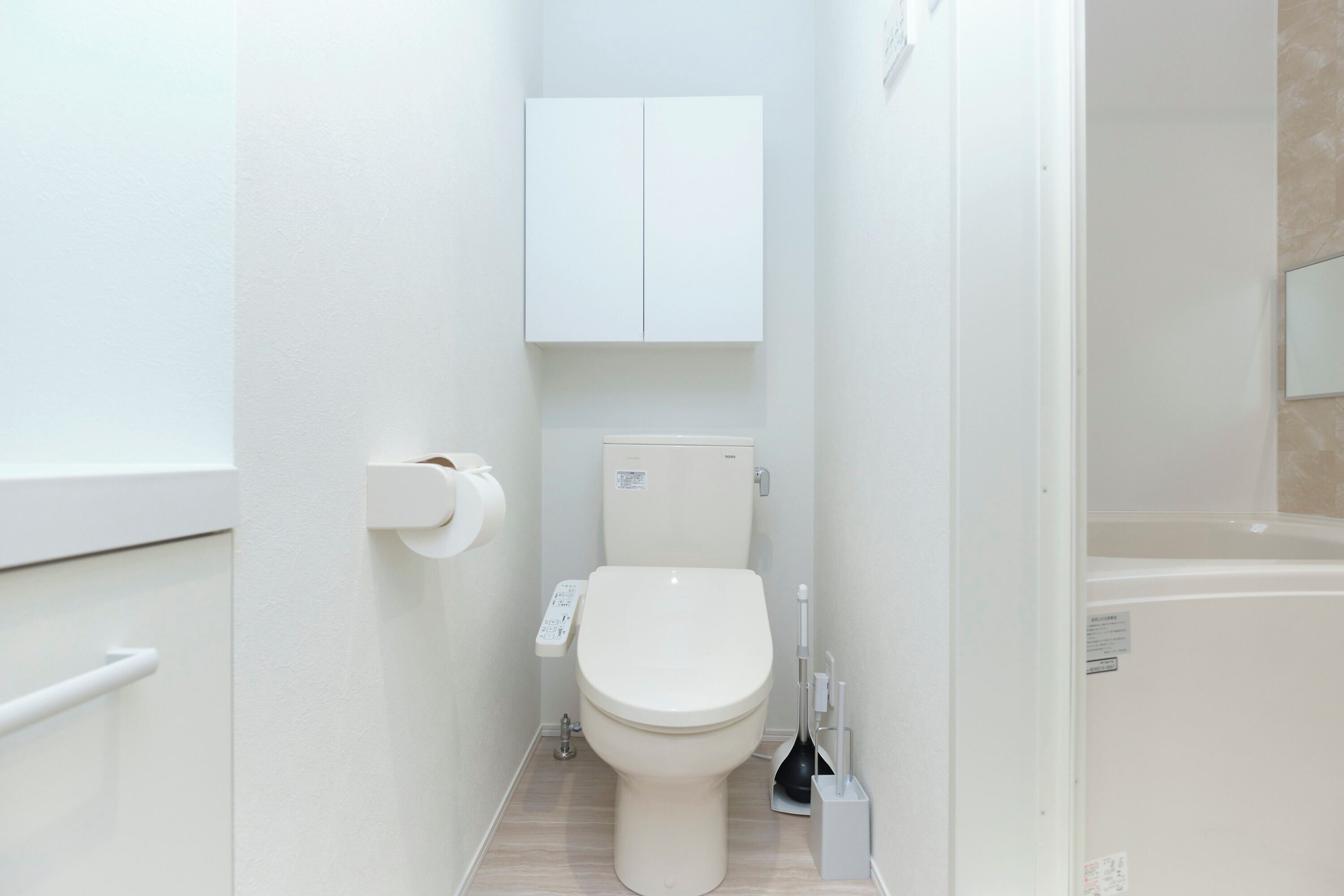 A small, modern bathroom with a toilet, a hand dryer, and a cabinet above the toilet.
