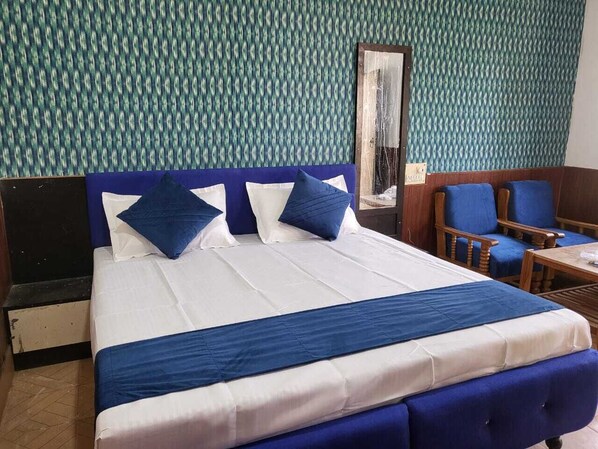 A hotel room with a large bed, blue and white bedding, a wooden headboard, and a patterned wall. - Avexia Funcity Resort (Mirzapur)