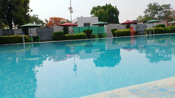 A swimming pool with clear water, surrounded by greenery and umbrellas. - Avexia Funcity Resort (Mirzapur)