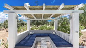 Ein überdachter Außenbereich mit weißem Pergola, integrierten Bänken und Blick auf die umliegende Landschaft.