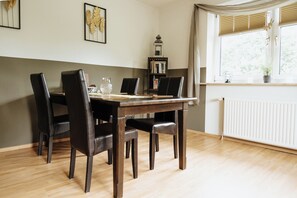 Et spiseområde med et træbord og stole, en reol og et vindue med persienner.