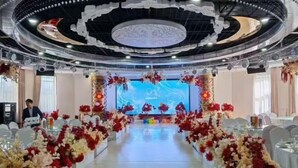 A banquet hall with a long table, floral decorations, and a large screen at the front. - Long Yin Tang Hotel (Xingyang)