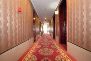 Un corridoio d'hotel con pareti decorate, tappeto rosso e porte su entrambi i lati.