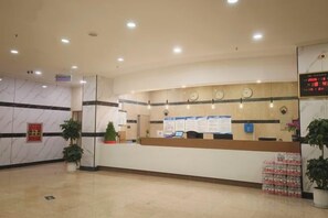 Zona reception di un hotel, con scrivania, orologio digitale e manifesti informativi.