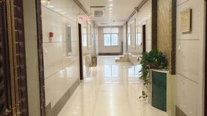 A hotel corridor with a polished floor, a reception desk, and a plant. - Long Yin Tang Hotel (Xingyang)