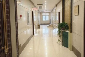 A hotel corridor with a polished floor, a reception desk, and a plant.