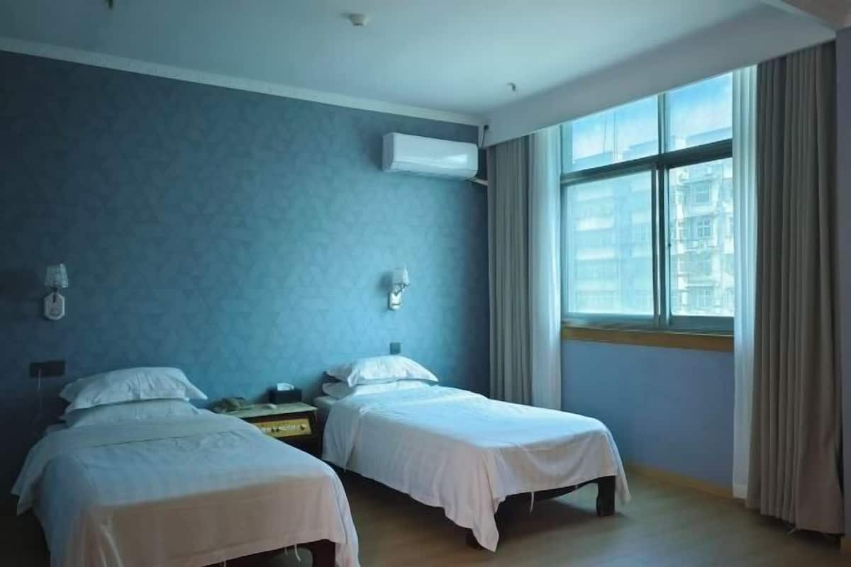 Habitación de hotel con dos camas, una ventana con cortinas y un equipo de aire acondicionado en la pared.