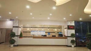 A reception area with a counter, digital display, and potted plants. - Long Yin Tang Hotel (Xingyang)