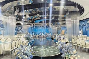 Ein runder Raum mit einem Glastisch in der Mitte, umgeben von weißen Stühlen, blauen floralen Dekorationen und einem blau gestalteten Hintergrund.