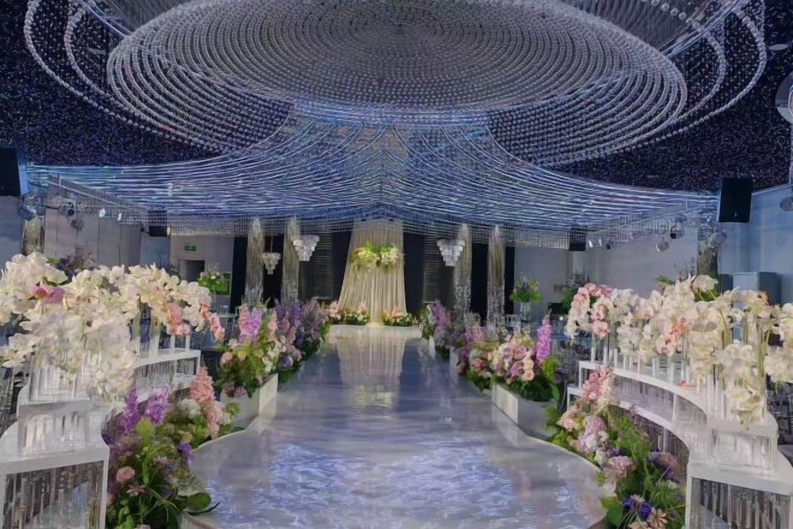 A venue with a central aisle flanked by floral arrangements and a ceiling with a circular light fixture.