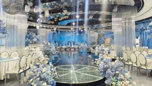 A circular room with a central glass table surrounded by chairs, a stage, and floral arrangements. - Long Yin Tang Hotel (Xingyang)