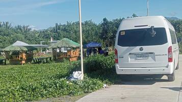 A white van parked on a paved area with a thatched-roof structure and wooden seating in the background.