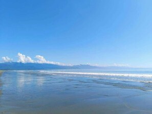 Une plage avec un ciel dégagé et des montagnes à l’horizon.