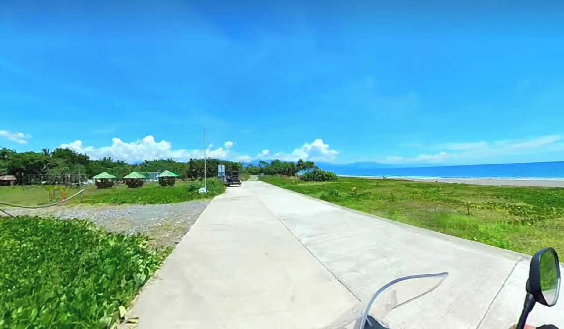 A paved pathway leading to a beach with green umbrellas and a clear blue sky.