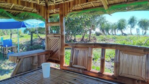 A wooden structure with a thatched roof, a table with a cup, and a view of palm trees and greenery. - The Waves at Socorro Baler- Hotel A (Baler)