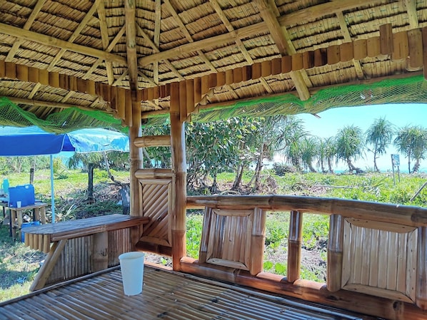 Estructura de madera con techo de paja, una mesa con una taza y vistas a palmeras y follaje.